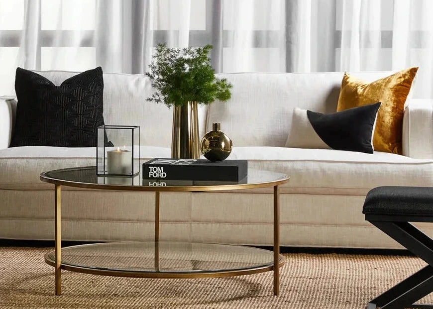 Modern living room with a white sofa, gold and black coffee table, and decorative pillows.