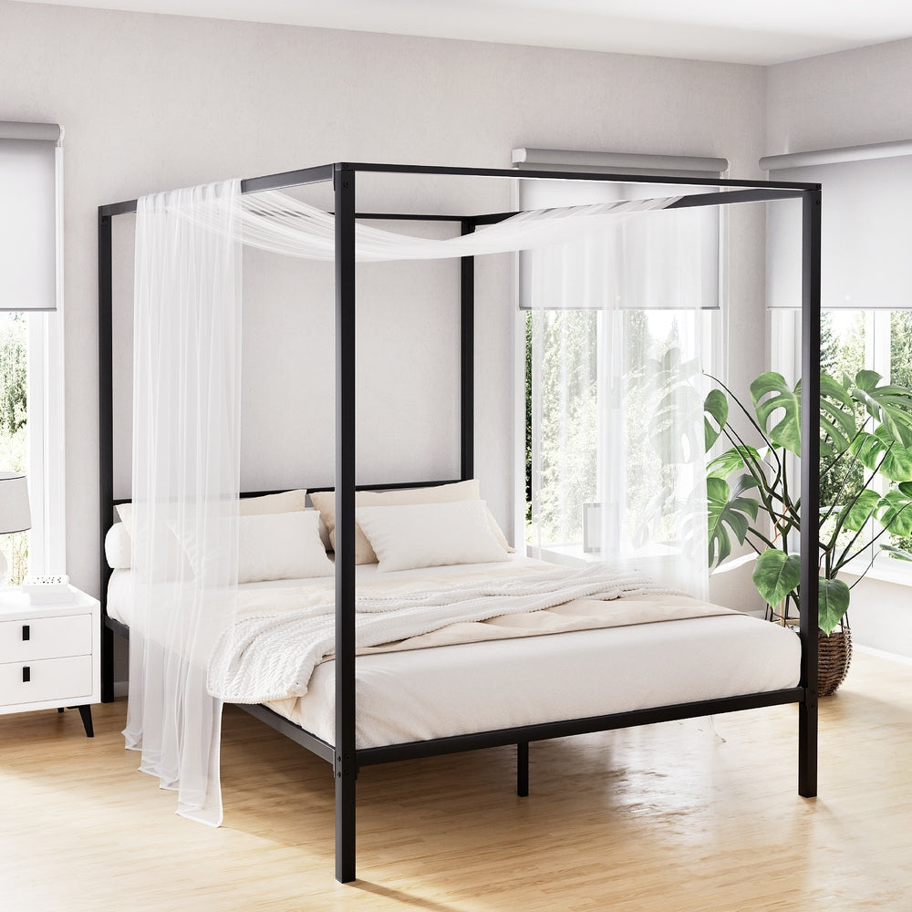 Black metal canopy bed with white bedding in a bright room with plants