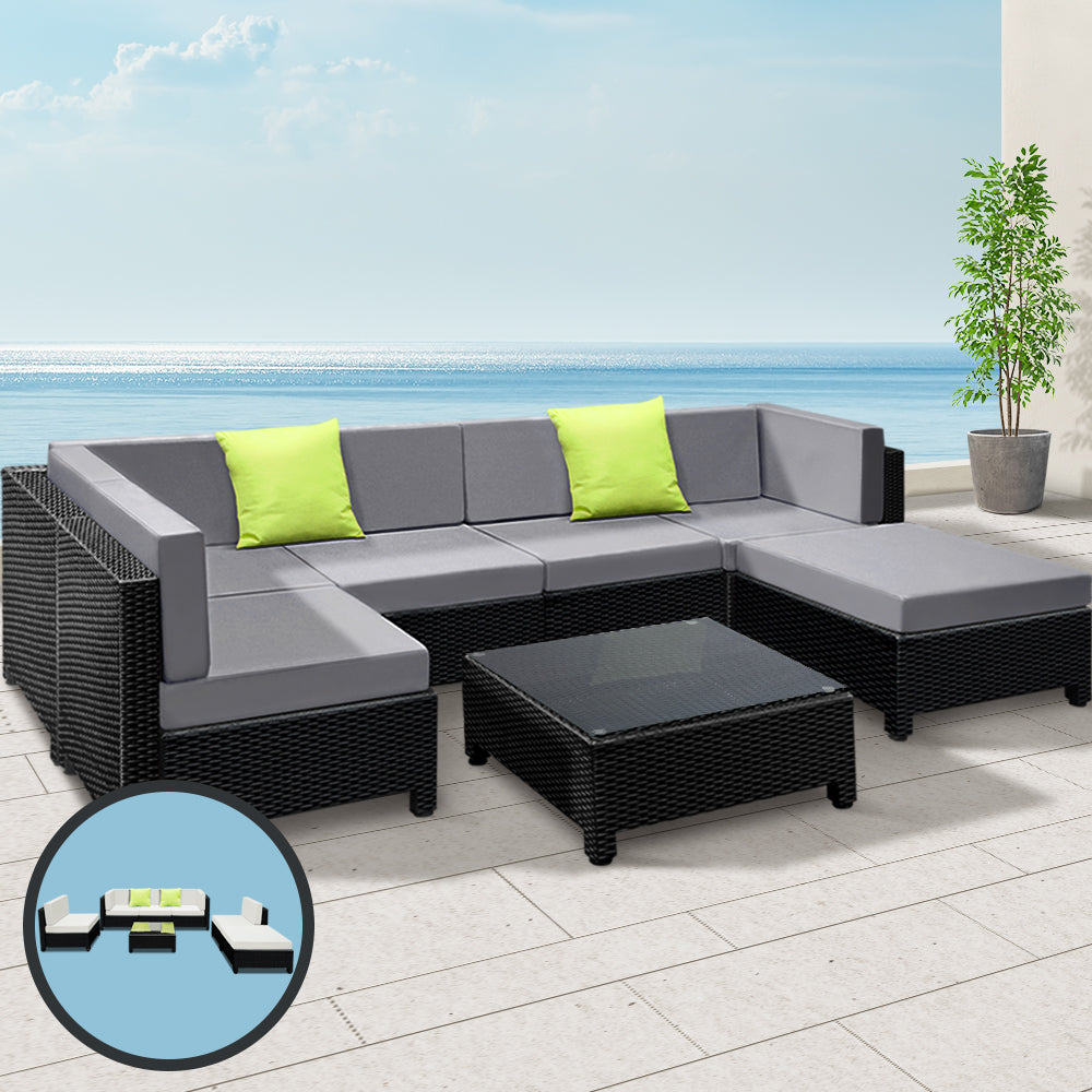 Outdoor patio furniture set with gray cushions and green pillows on a patio with ocean view.