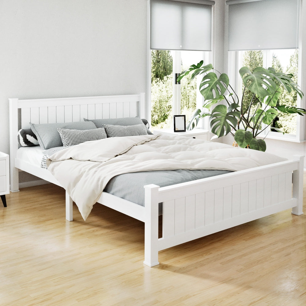 White wooden bed in a bright bedroom with plants and a window.